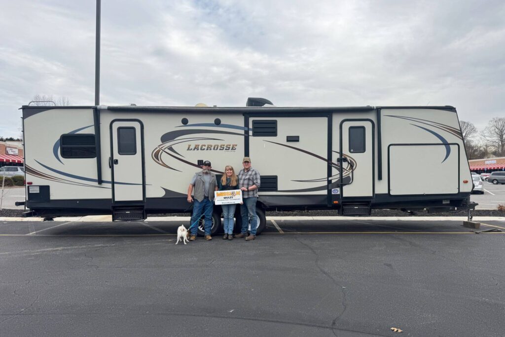 Three people standing in front of a long RV