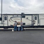 Three people standing in front of a long RV
