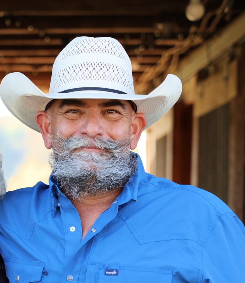 Bearded man wearing white cowboy hat and blue Wrangler shirt