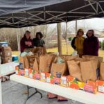 Women standing under a tent with filled grocery bags