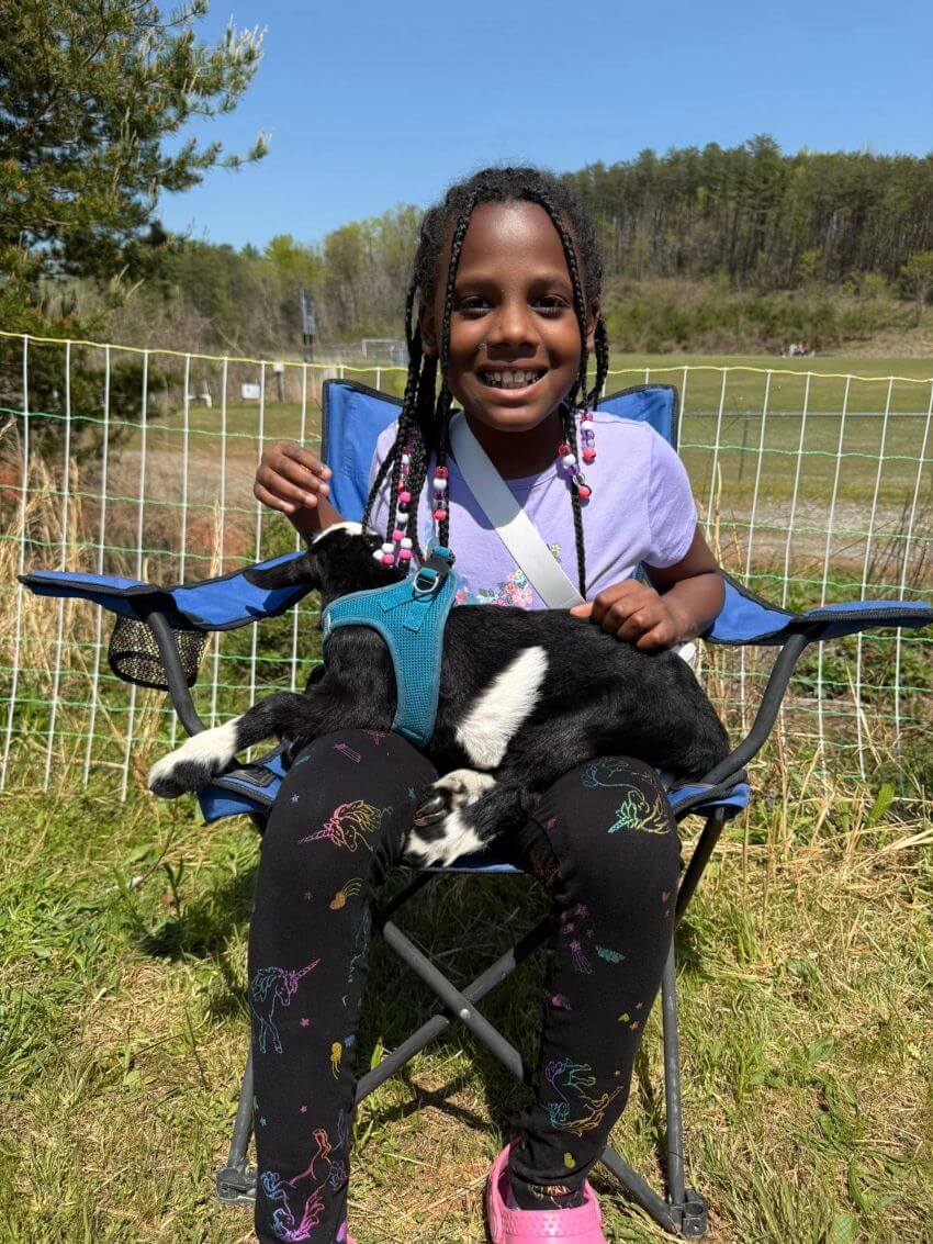 Young black girl on blue chair holding a baby goat