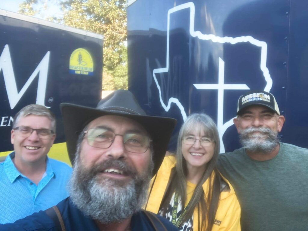 3 men and a woman smiling for a selfie in front of a truck